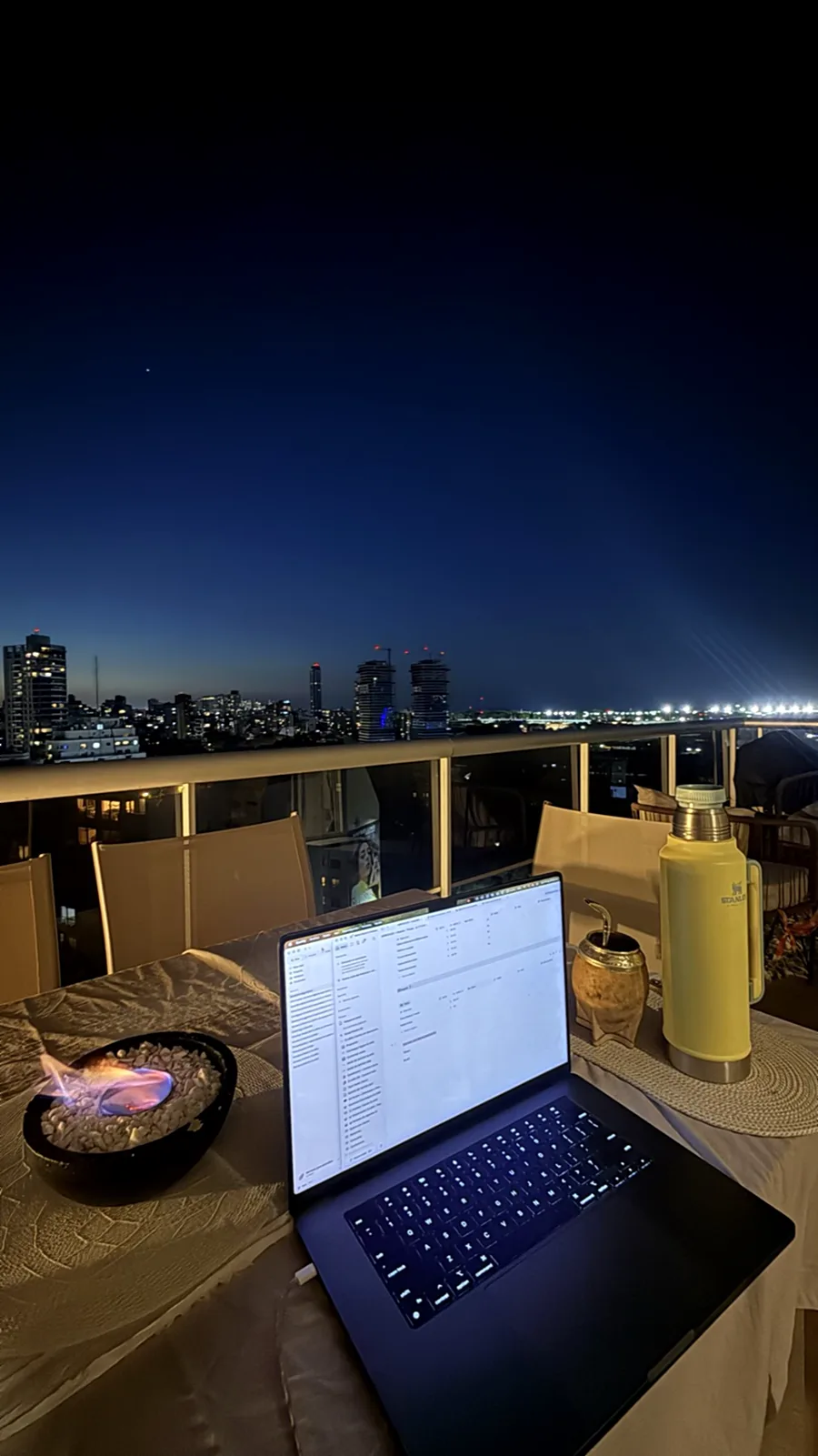 Su laptop en la terraza de noche, con las luces de la ciudad